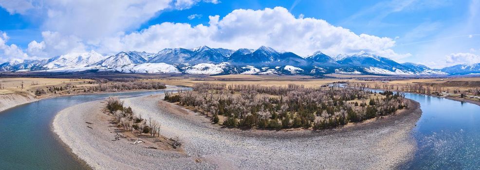 Image of Panorama of river curving around spring forest with stunning mountain covered in snow on horizon