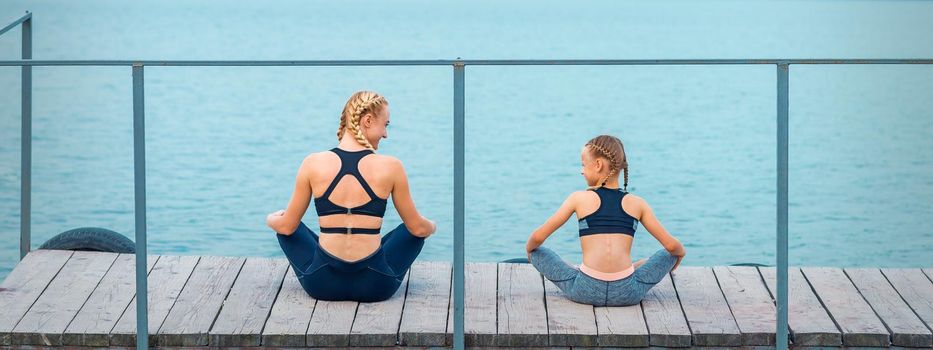 Mother and daughter doing gym exercises on the grass at the pier of the river