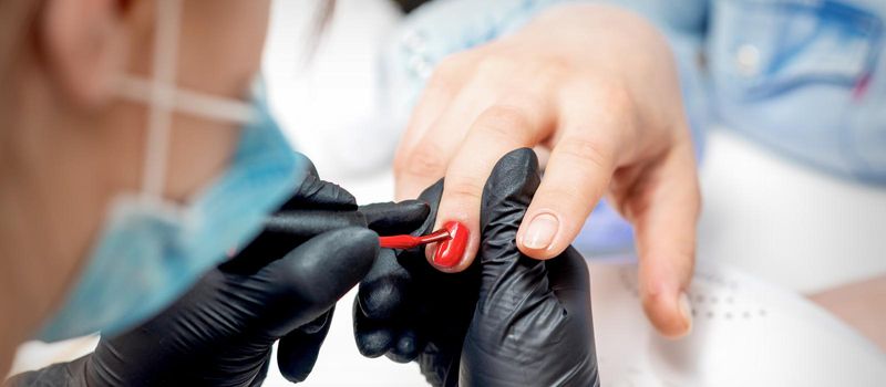 Professional manicure master painting female nails by red nail polish in nail salon