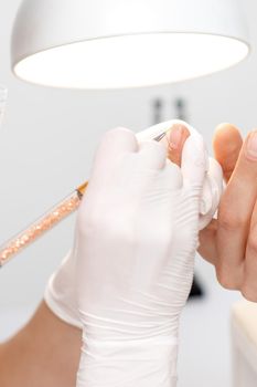 Professional manicure master drawing decorations by pink gel pencil on edge of a nail of young female