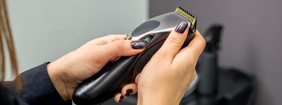 Hair clipper in hands of female professional hairdresser or barber in hair salon