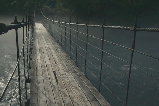 old wooden long suspension bridge over the Belaya mountain river, in nature, thick mystical fog over the water at night in the moonlight