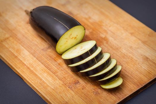 Fresh sliced eggplant on wooden cutting board isolated on black. Cooking ingredients