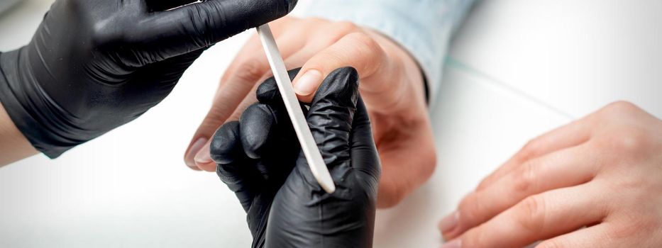 Closeup shot of young woman getting manicure by manicure master with nail file in nail salon