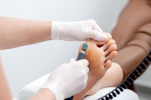 Peeling feet pedicure procedure from callus on foot by hands of podiatrist in white gloves at beauty salon