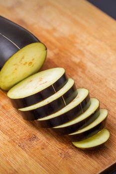 Fresh sliced eggplant on wooden cutting board isolated on black. Cooking ingredients
