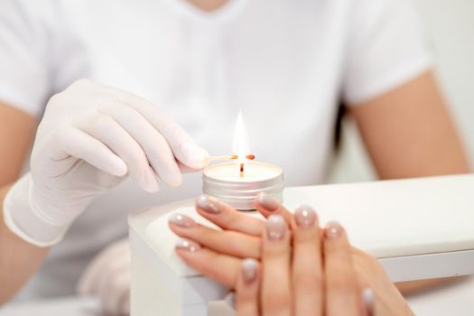 Manicure master in white gloves lighting candle with match in nail salon