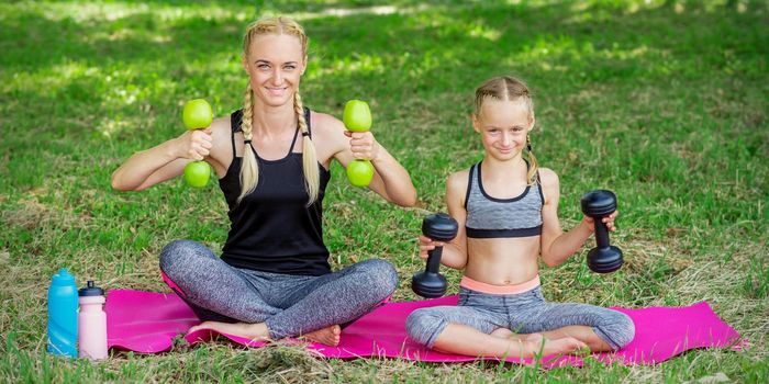 Young woman and girl are training with dumbbells sitting on the grass in the park