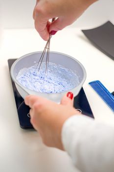 Hairdresser is mixing dye in white bowl for hair coloring in her hands