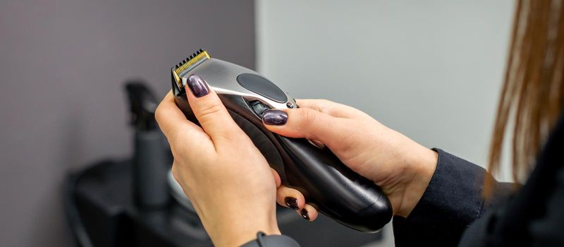 Hair clipper in hands of female professional hairdresser or barber in hair salon