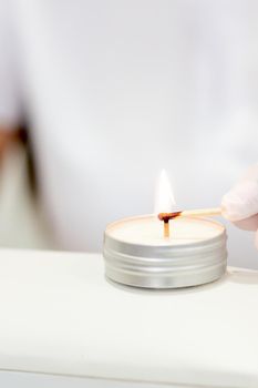 Manicure master in white gloves lighting candle with match in nail salon