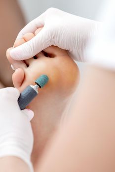 Peeling feet pedicure procedure from callus on foot by hands of podiatrist in white gloves at beauty salon