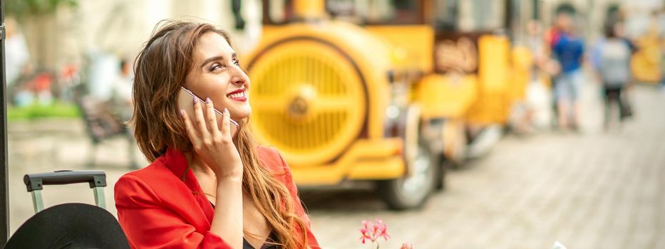 Beautiful happy young caucasian woman talking by cell phone sitting in outdoors cafe at european city