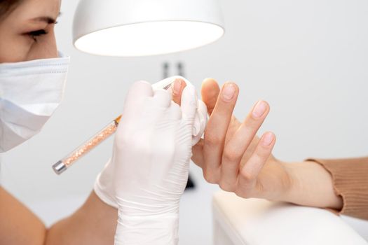 Professional manicure master drawing decorations by pink gel pencil on edge of a nail of young female