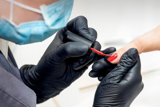 Professional manicure master painting female nails by red nail polish in nail salon