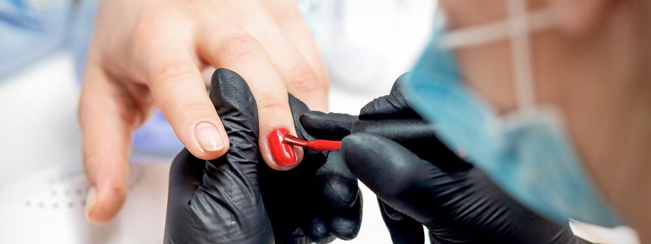 Professional manicure master painting female nails by red nail polish in nail salon
