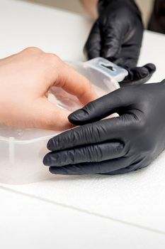 Soaking fingernails in the bath with water on white table under the supervision of a manicurist