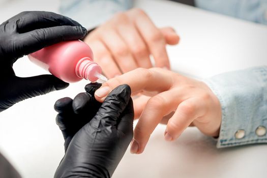 Nail treatment by cuticle oil while manicure of young woman in nail salon