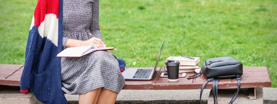 Student young woman is writing notes to diary on the bench in the park