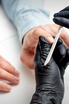 Closeup shot of young woman getting manicure by manicure master with nail file in nail salon