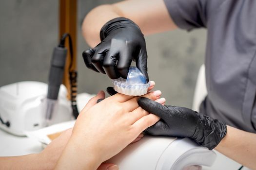 Manicure master is brushing dust from female fingernails in nail salon