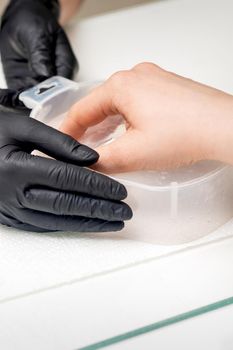 Soaking fingernails in the bath with water on white table under the supervision of a manicurist