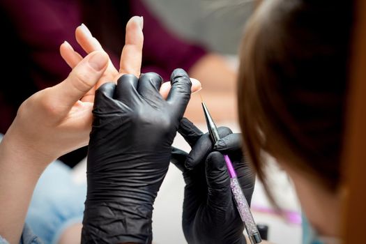 Manicure master is painting decorations by purple gel pencil on edge of female nail in nail salon
