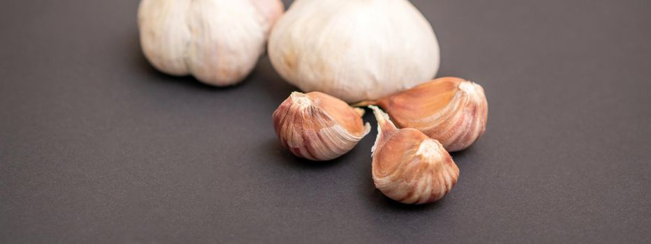 Still life of two garlic heads and garlic cloves grouped on dark background
