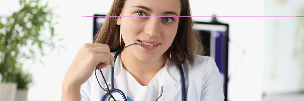 Portrait of attractive young doctor posing in personal office in clinic. Intern wait for next patient on appointment wear stethoscope. Healthcare concept