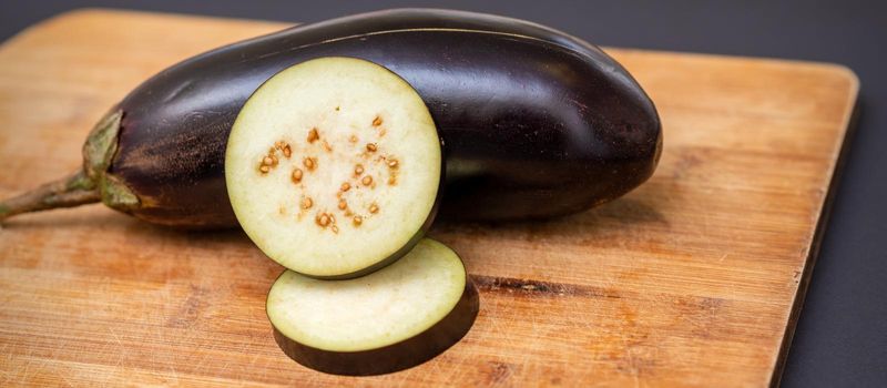 Fresh sliced eggplant on wooden cutting board isolated on black. Cooking ingredients