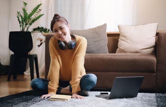 smiling girl looking at the camera Beside the laptop sit on the floor in front of the sofa and put on headphones. vacation at home.