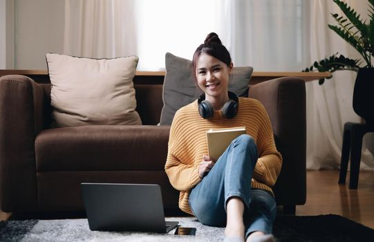 Portrait of a happy beautiful woman looking at the camera listening to music in headphones from her smartphone on the sofa floor at home..