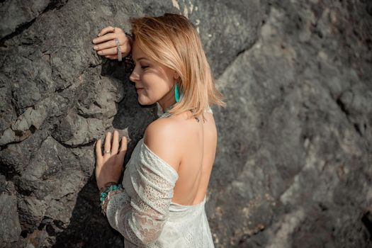 Middle aged woman looks good with blond hair, boho style in white long dress on the beach decorations on her neck and arms