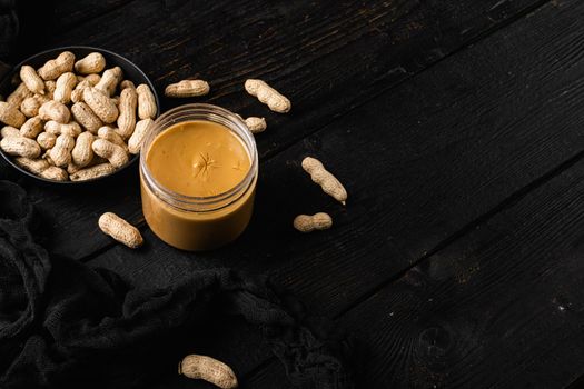 Fresh made creamy Peanut Butter set, on black wooden table background, with copy space for text