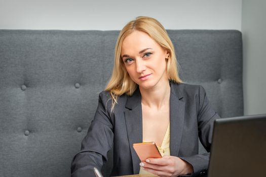 Portrait of beautiful young caucasian businesswoman with smartphone working in office looking at camera