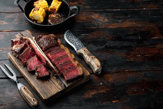 Grilled medium rare t bone or Porterhouse steak set, on wooden serving board, on old dark wooden table background, with copy space for text