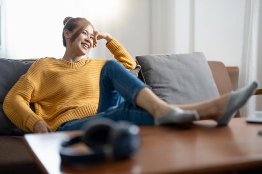 Relaxing home lifestyle happy asian woman in relax room sofa lying back with arms behind head smiling. Asian girl in comfortable lounging chair travel living