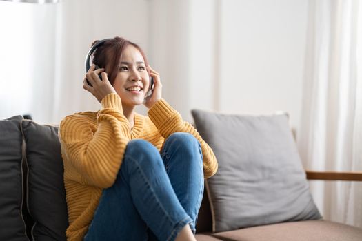 Freelance asian woman with mobile phone listening music in headphones and relax at home. Happy girl sitting on couch in living room