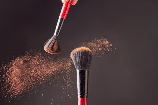 Two make-up brushes with brown powder splashes. Spraying of cosmetic powder in motion.