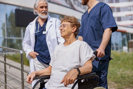 Nurse and doctor talking to patient on wheelchair in hospital yard . Rehabilitation concept.