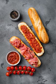 Crusty toast with fresh tomatoes and cured ham, on gray stone table background, top view flat lay