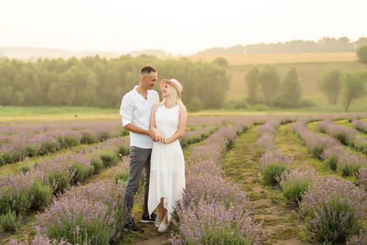 A loving couple standing in a lavender field and hugging.