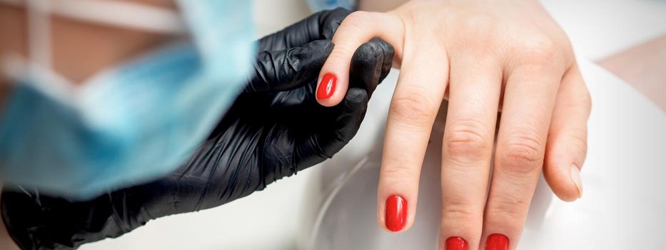 Young woman receives red nail polish by professional manicure master in nail salon