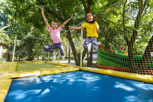 Two little girls in the summer jump on a trampoline, smiling and laughing. Children play. Relax in the fresh air. Friends jump on a trampoline. Happy child.