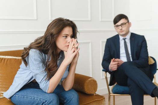 A young woman at a psychiatrist's or psychologist's appointment is worried, holds her hands to her face and tries to talk about her problems