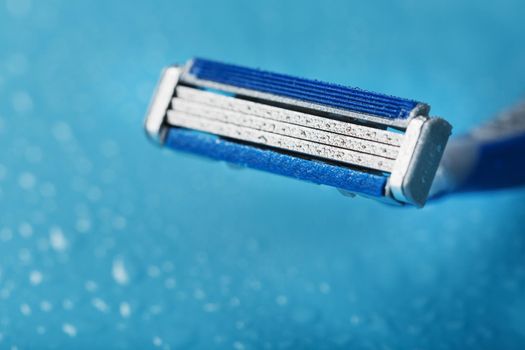 Shaving machine with three blades on a blue background with water drops in close-up. The concept of purity and freshness