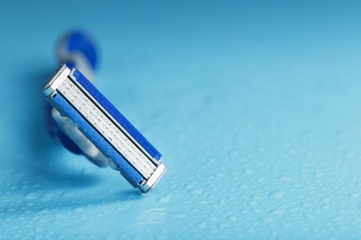 Shaving machine with three blades on a blue background with water drops in close-up. The concept of purity and freshness