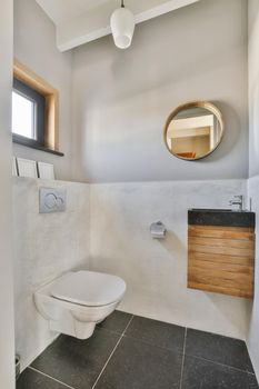 Modern flush toilet and ceramic sink installed on white tiled walls near mirror and towel in small restroom at home