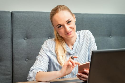 Portrait of beautiful young caucasian businesswoman with smartphone working in office looking and smiling at camera
