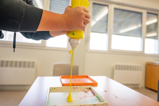 Worker squeezing yellow paint from tube into tray to prepare it for painting